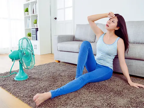 Woman feeling overheated on the floor with fan running due to broken air conditioner